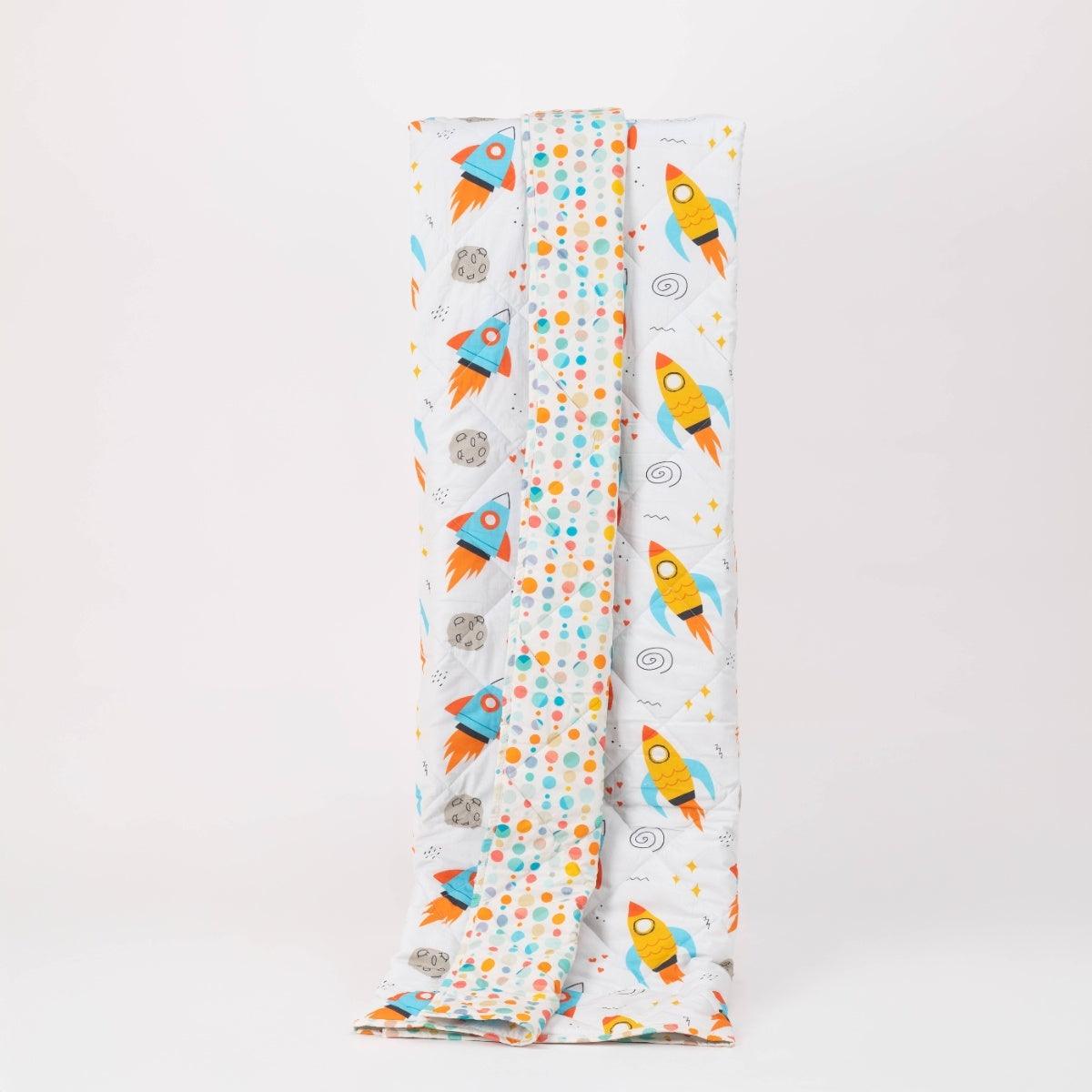 Reversible quilted kids blanket with outer space-themed print featuring stars, planets, and rockets.