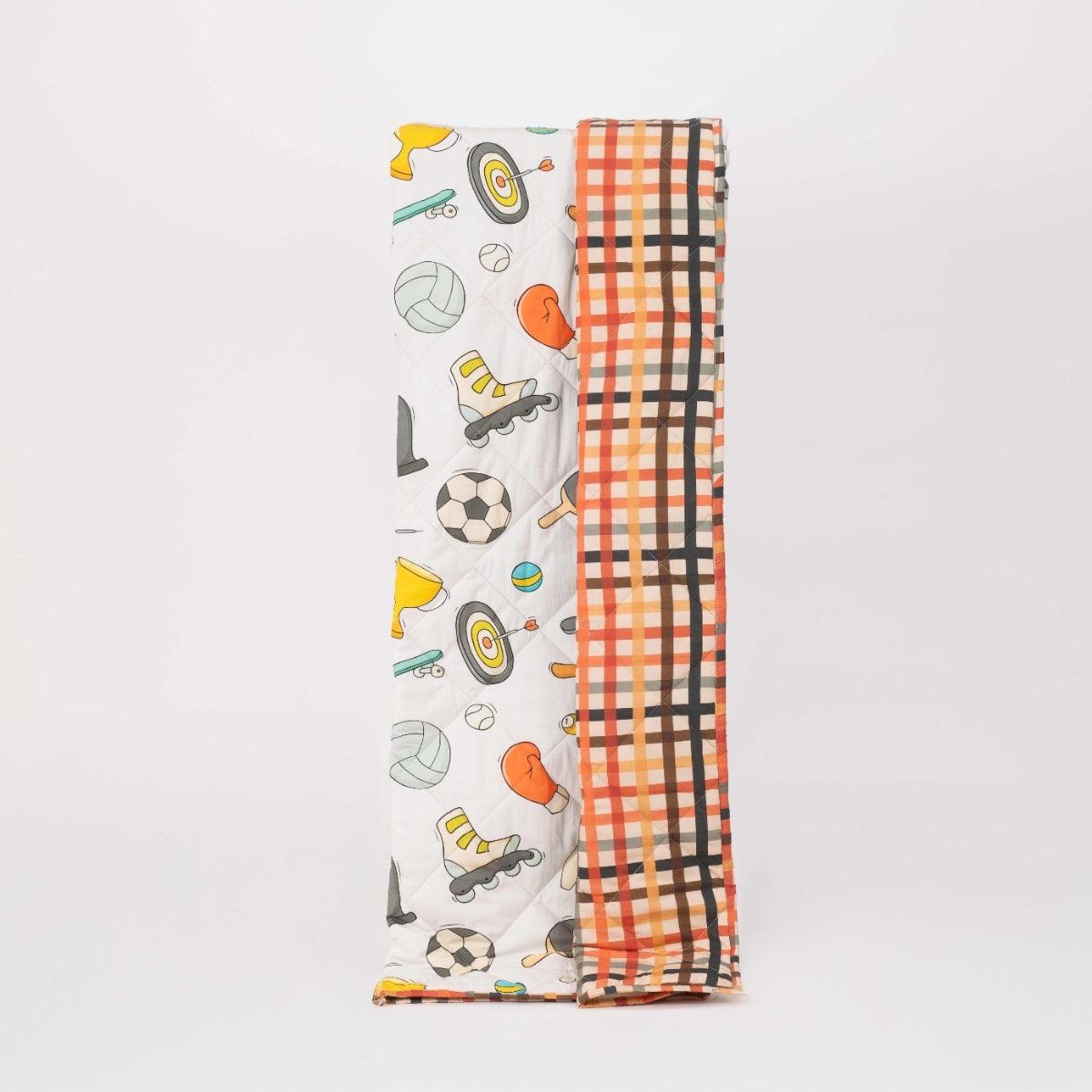 Playful Plunge kids comforter with sport-themed print featuring balls and equipment, shown laid out on a bed with soft stitching detail
